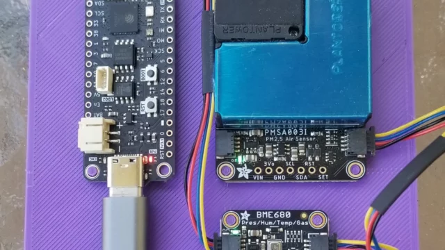A plastic 3D-printed plate on which three circuit boards are placed. The Feather S3 board is on the left side, oriented so the long edge is vertical. The PMSA003i is placed in the upper right quadrant. The BME680 is placed below the PMSA003i. STEMMA QT cables connect all 3 boards to one another. A USB-C cable connected to the Feather S3 disappears off the bottom of the photo.